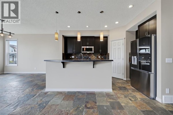 Open concept kitchen with dark wood cabinets, granite countertops, and a large island. - 151 Copperfield Common Se, Calgary