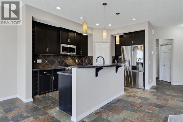 Kitchen island with seating and dark wood cabinets, granite countertops, and stainless steel appliances. - 151 Copperfield Common Se, Calgary