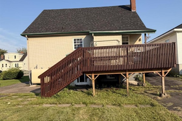 Rear view of the cream-colored house showing a large dark brown deck with stairs and a water tank on the side. - 151 Gray Street, Sydney