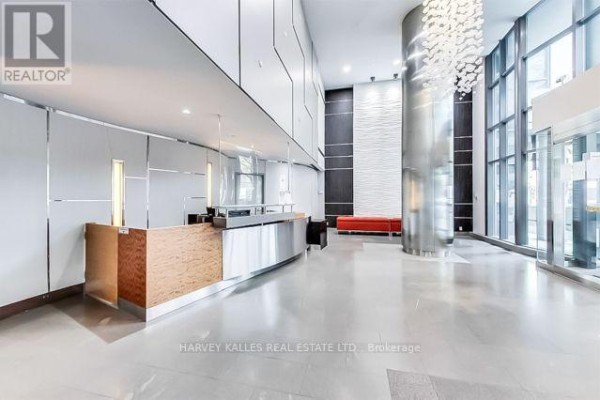 Modern lobby with stainless steel reception desk, columns, and red bench. - 1510 - 361 Front Street W, Toronto