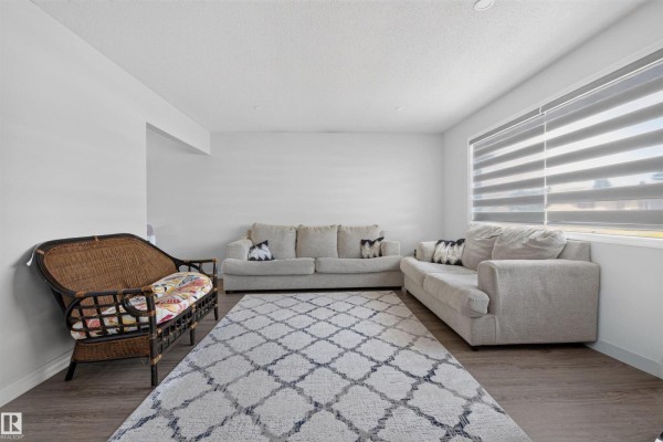 Living room with two grey sofas, a wicker chair, and a patterned area rug on wood-look flooring. - 15104 74 St Nw, Edmonton