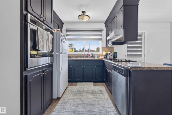 Kitchen with dark cabinets, granite countertops, stainless steel appliances, and a window over the sink. - 15104 74 St Nw, Edmonton