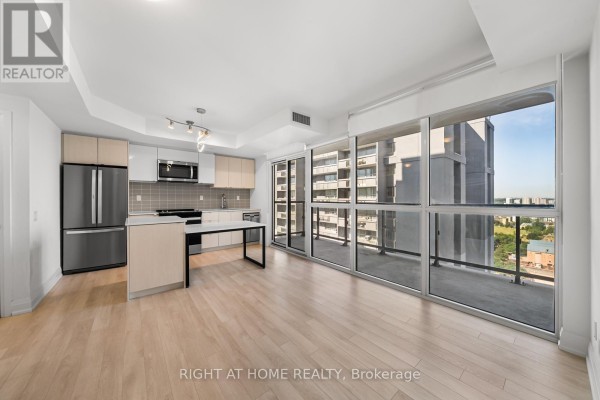 Living area and kitchen with floor-to-ceiling windows and balcony overlooking city buildings. - 1511 - 1461 Lawrence Avenue, Toronto