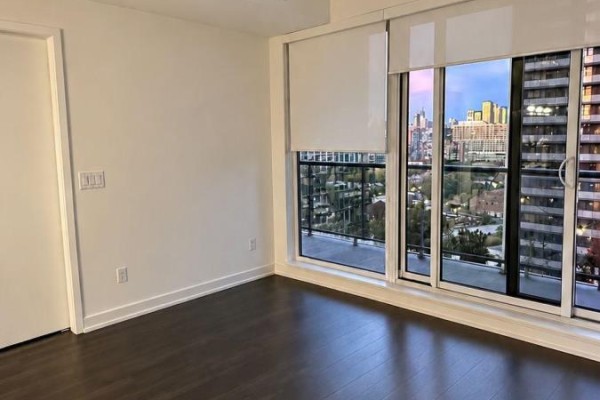 Empty room with dark hardwood floors and large windows overlooking a cityscape. - 1511 - 25 Ordnance Street, Toronto