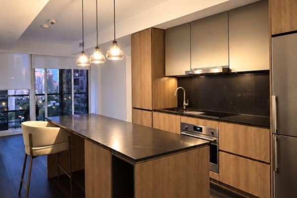 Kitchen with wood cabinetry, a dark stone island, stainless steel appliances, and pendant lights. - 1511 - 25 Ordnance Street, Toronto