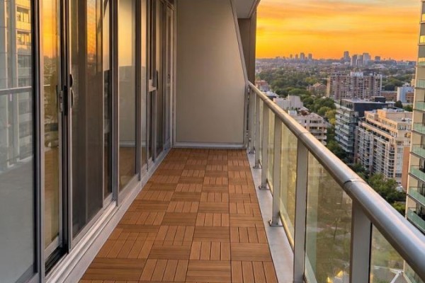 Balcony with wood tile flooring, glass railings, and a panoramic view of the city at sunset. - 1511 - 25 Ordnance Street, Toronto