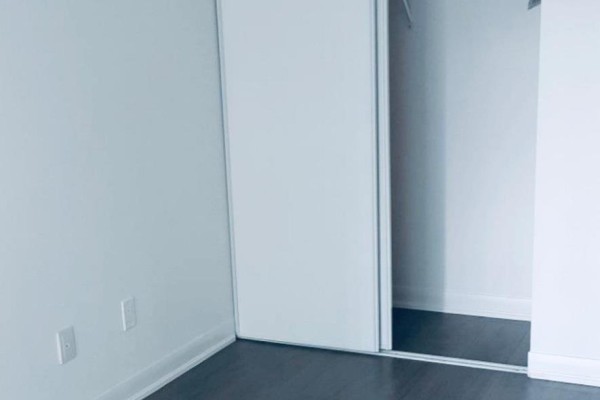 Bedroom corner with white walls, dark wood floors, and a sliding mirrored closet. - 1511 - 5162 Yonge Street, Toronto