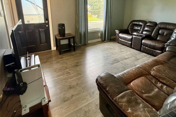Living room with a brown leather sofa and a view of the front door and a window with grey curtains. Light wood-look vinyl flooring. - 1511 Grandview Street W, Moose Jaw