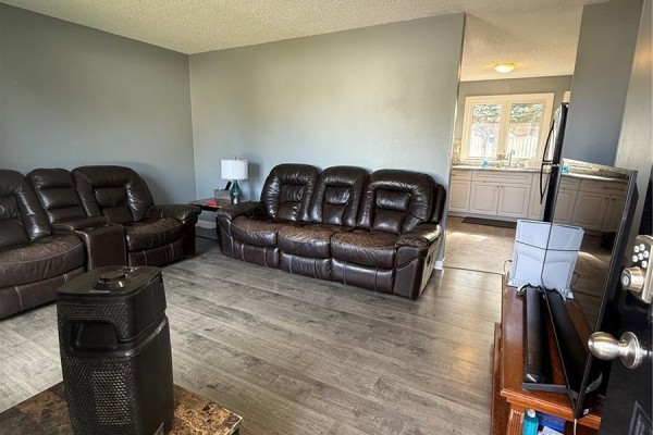 Living room with brown leather sofas and an open doorway leading to a kitchen with light grey cabinets and countertops. - 1511 Grandview Street W, Moose Jaw