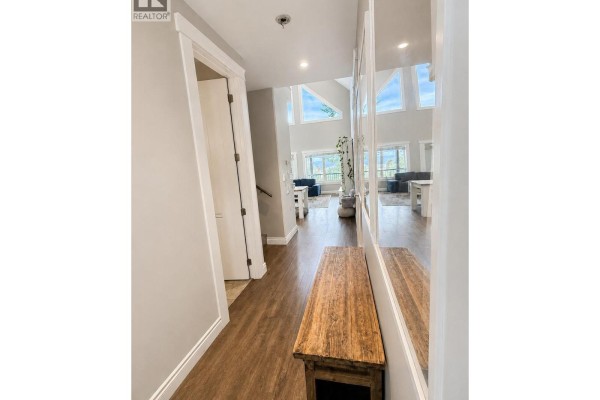 Hallway with wood floors, a wooden bench, and a view into a living room with large windows. - 1511 Mount Royal Ridge, Cranbrook