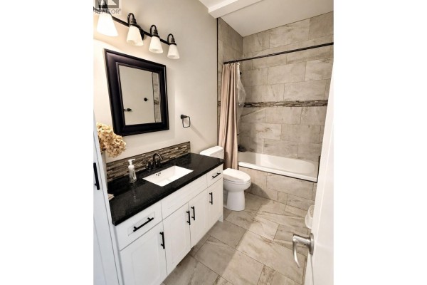 Bathroom with a white vanity, black granite countertop, white toilet, and a tiled shower/tub combination. - 1511 Mount Royal Ridge, Cranbrook