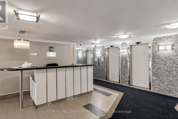 Apartment living area with dark wood floors, white walls, showing a kitchen entrance and balcony access. - 1512 - 15 Kensington Road, Brampton