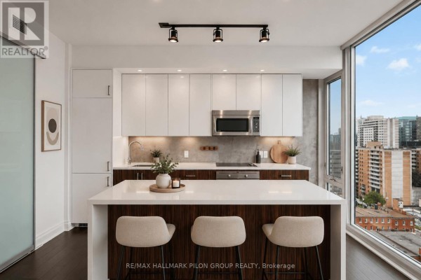 Modern kitchen with white and wood cabinets, an island with bar stools, and city views. - 1512 - 300 Lisgar Street, Ottawa