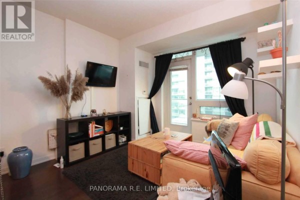 Living room showing a sofa, coffee table, television, black shelves, and balcony access. - 1512 - 55 East Liberty Street, Toronto
