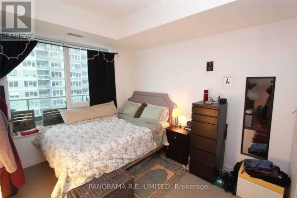 Bedroom with a queen-size bed, nightstand, dresser, mirror, and large window with city view. - 1512 - 55 East Liberty Street, Toronto