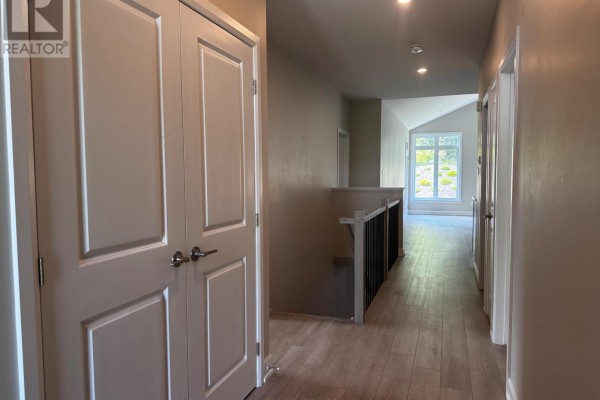 Interior hallway with beige walls, wood flooring, and double closet doors. - 1513 Flanders Road, Brockville