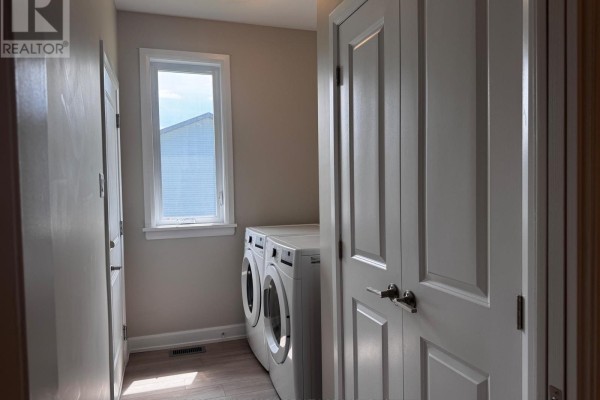 Laundry room with white washer and dryer, beige walls, and a small window. - 1513 Flanders Road, Brockville