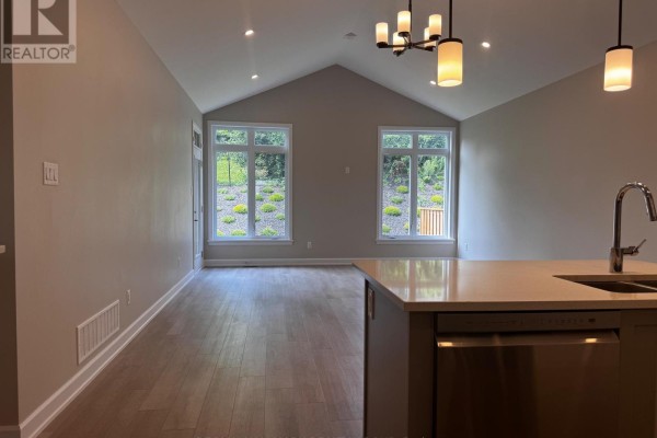 Living room with vaulted ceiling, large windows, and a kitchen island in the foreground. - 1513 Flanders Road, Brockville