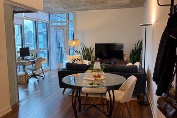 Apartment living area with a desk, sofa, coffee table, and a coat rack by the door. - 1514 - 210 Simcoe Street, Toronto