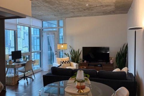 Apartment living area with a desk, sofa, coffee table, and a coat rack by the door. - 1514 - 210 Simcoe Street, Toronto