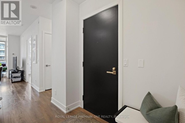 Apartment hallway with wood flooring, dark door, and a bench with green cushions. - #1514 - 9471 Yonge Street, Richmond Hill