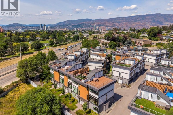 Modern kitchen with white and wood cabinets, a large island with bar stools, and stainless steel appliances. - 1515 Highland Drive N Unit# 29, Kelowna