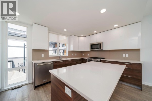 Kitchen and dining area with white and wood cabinets, an island, and a round dining table. - 1515 Highland Drive N Unit# 29, Kelowna