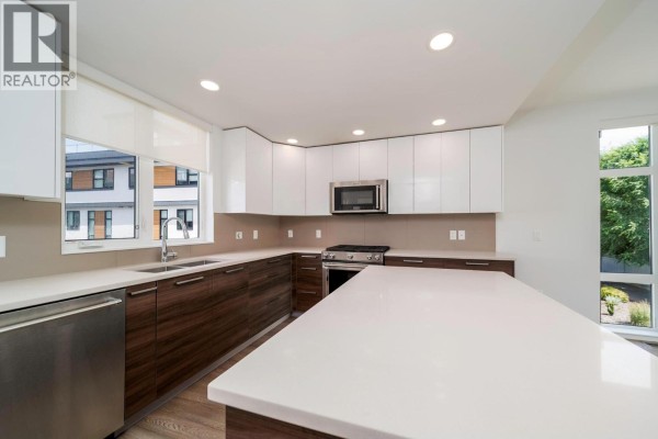 Living room with a large grey sectional sofa, mounted TV, and expansive windows with a view. - 1515 Highland Drive N Unit# 29, Kelowna