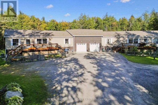 Front view of a beige multi-family home with two garages and multiple wooden decks, surrounded by trees. - 1515 Uffington Road, Bracebridge