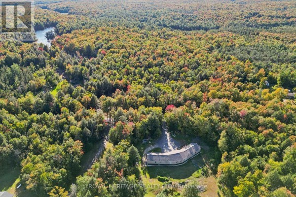 Aerial view of a property surrounded by trees and woods, with a body of water visible in the distance. - 1515 Uffington Road, Bracebridge