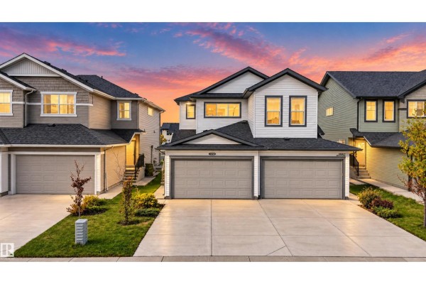 Exterior of a duplex at dusk, showing warm interior lights against a colorful sky. - 15150 26 St Nw Nw, Edmonton