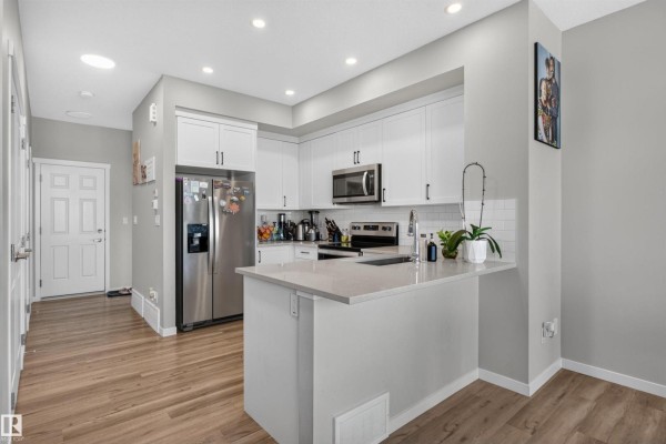 Open concept kitchen with white cabinets, stainless steel appliances, and a breakfast bar. - 15150 26 St Nw Nw, Edmonton