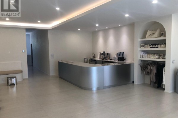 Commercial interior with a curved silver reception desk, coffee machine, and retail shelving with clothing. - 1517-1519 O Connor Drive, Toronto