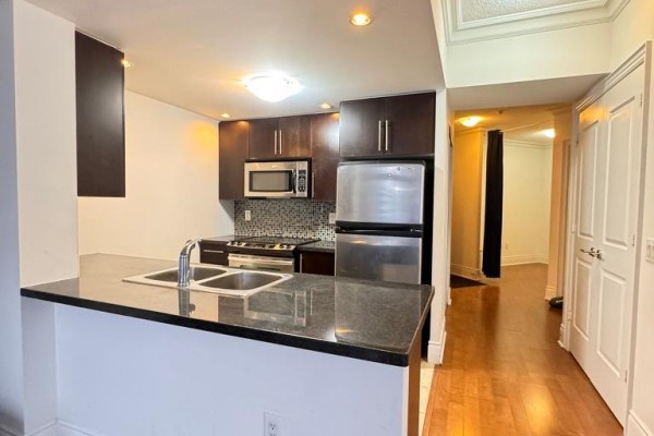 Kitchen with dark wood cabinets, granite countertop, stainless steel appliances and hardwood floors. - 1519 - 500 Doris Avenue, Toronto