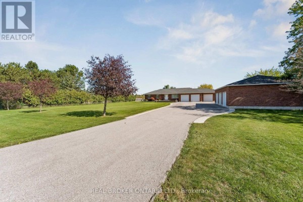 Asphalt driveway leading to a long red brick bungalow with a detached garage on the right. - 15191 Airport Road, Caledon