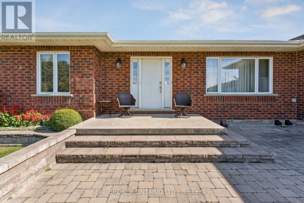 Front entrance of the red brick house with a paved walkway, steps, and two chairs. - 15191 Airport Road, Caledon