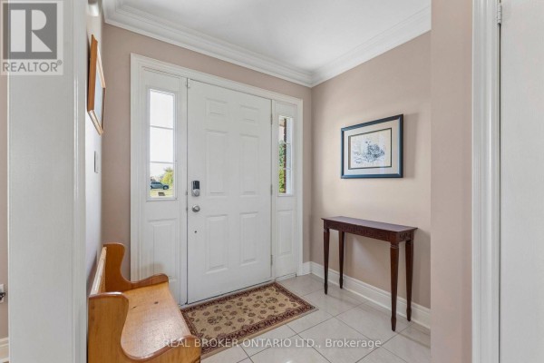 Interior view of the front entrance with a white door, beige walls, wood bench, and console table. - 15191 Airport Road, Caledon