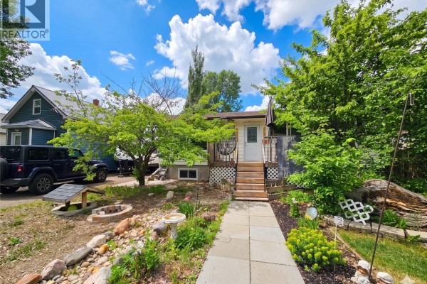 Front view of a small house with a walkway, trees, and a fire pit. - 152 5th Avenue Se, Swift Current