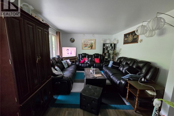 Living room with multiple black leather sofas, a coffee table, and a large dark wood cabinet. - 152 5th Avenue Se, Swift Current