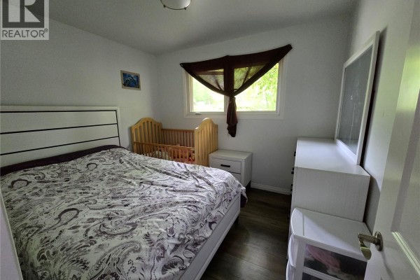 Bedroom with a king-size bed, a crib, a white dresser, and a window. - 152 5th Avenue Se, Swift Current