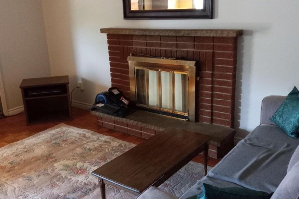 Living room featuring a brick fireplace, wood floor, sofa, and coffee table. - 152 Beech Street, Brampton