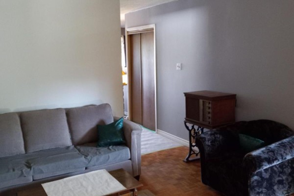 Living room with grey sofa, armchair, and a wooden antique radio on a stand. - 152 Beech Street, Brampton