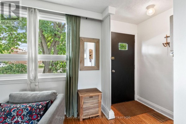 Interior entryway with wood floor, black door, white walls, and large window with green curtains. - 152 Harmony Road S, Oshawa