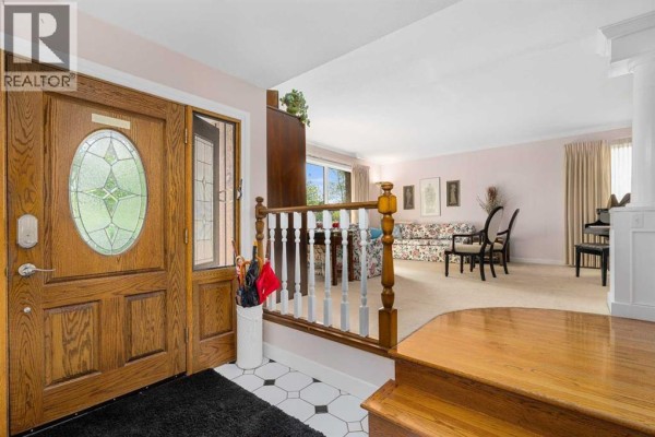 Entrance foyer with a wooden front door, black and white tile floor, and view of a living room. - 152 Templewood Road Ne, Calgary