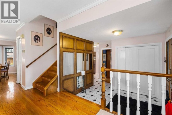 Interior view of a hallway with hardwood floors, wooden staircase, mirrored panel, and white closet doors. - 152 Templewood Road Ne, Calgary