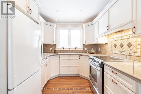 Kitchen with white cabinets, tile backsplash, stainless steel stove, and hardwood floor - 1520 Rosemount Road Tay