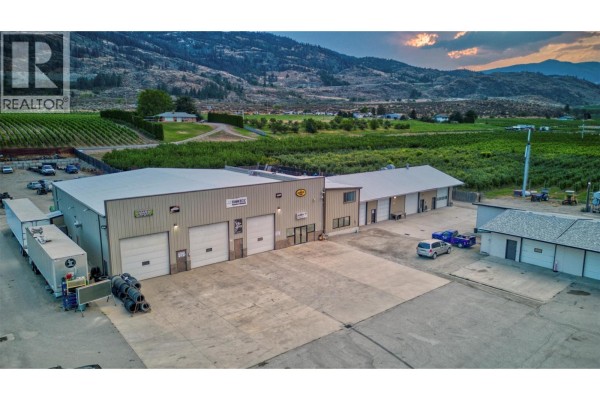 View of commercial buildings and outdoor storage areas with orchards in the distance. - 15210 97 Highway, Osoyoos