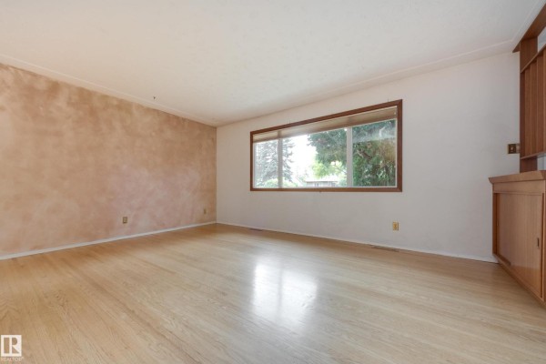 Living room with light wood floor, textured peach walls, and a large window. - 15216 86 Av Nw, Edmonton