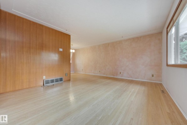 Interior view of a spacious living area with light wood floors and wood paneling. - 15216 86 Av Nw, Edmonton