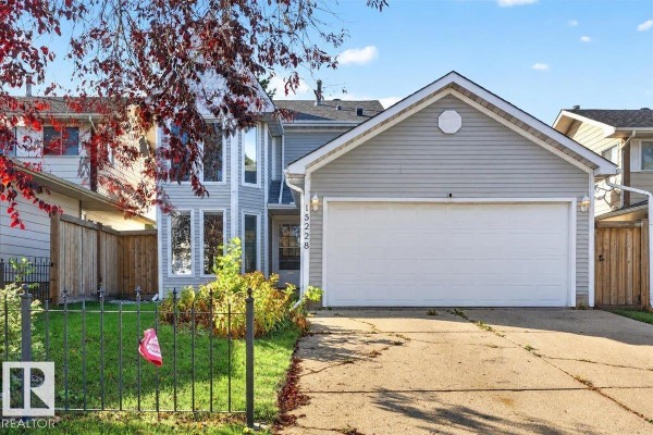 Front view of a light blue house with a large white garage door and a concrete driveway. - 15228 84 St Nw, Edmonton